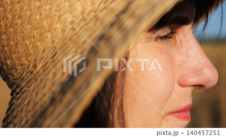 Female farmer in straw hat looking into wheat field and examining plantation at sunset. Close up face of adult beautiful woman illuminating by bright rays of sun. Concept of agriculture business Female farmer in straw hat looking into wheat field and examining plantation at sunset. Close up face of adult beautiful woman illuminating by bright rays of sun. Concept of agriculture business 140457251