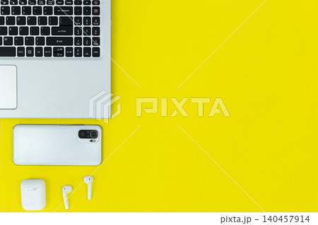 Bright yellow background with tech essentials. Glasses rest beside a laptop and wireless earbuds. Minimalist workspace conveys calm and focus. Perfect for digital design, startup Bright yellow background with tech essentials. Glasses rest beside a laptop and wireless earbuds. Minimalist workspace conveys calm and focus. Perfect for digital design, startup 140457914
