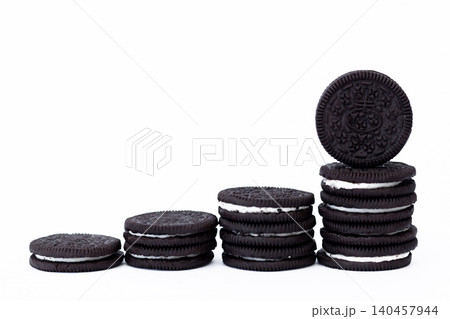 Stack of cookies, one resting atop. Dark, round, crisp, with cream filling. Clean, isolated, studio-lit background. Ideal for food, snack, dessert, or advertising 140457944
