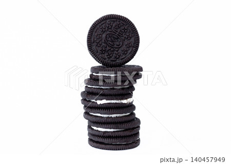 Stack of cookies, one resting atop. Dark, round, crisp, with cream filling. Clean, isolated, studio-lit background. Ideal for food, snack, dessert, or advertising 140457949