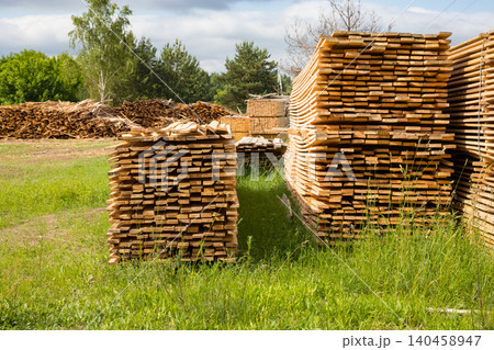 Stacked wooden planks at lumber industry yard, sawn timber boards stored at sawmill enterprise outdoor on grass 140458947