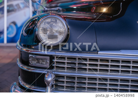 Closeup view of a black vintage luxury car with round headlight and polished chrome grille details. Historic retro automobile displayed indoors highlights elegant automotive craftsmanship and classic 140458998
