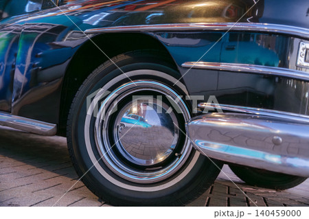Detailed closeup of a vintage classic car wheel with chrome hubcap and polished bumper reflections. Historic automobile highlights retro transportation style and restored automotive design. Detailed closeup of a vintage classic car wheel with chrome hubcap and polished bumper reflections. Historic automobile highlights retro transportation style and restored automotive design. 140459000
