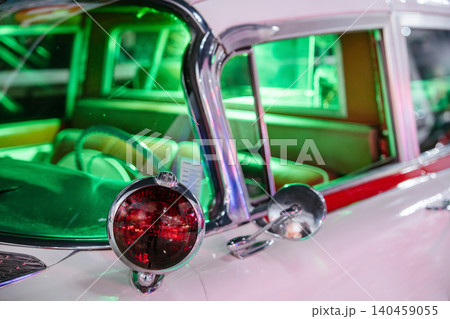 Close-up shot highlights exterior of vintage car showcasing chrome accents and round red taillight. Interior illuminated by vibrant green light reveals plush seating, evoking retro nostalgia. Close-up shot highlights exterior of vintage car showcasing chrome accents and round red taillight. Interior illuminated by vibrant green light reveals plush seating, evoking retro nostalgia. 140459055