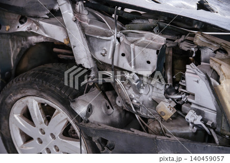 Detailed close-up view of front section of car wreckage after accident. Crumpled metal and exposed engine components highlight extent of damage, with tire amidst wreckage. Detailed close-up view of front section of car wreckage after accident. Crumpled metal and exposed engine components highlight extent of damage, with tire amidst wreckage. 140459057