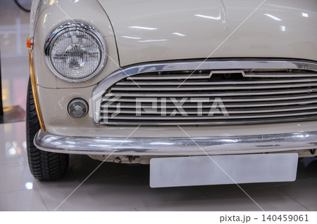 Detailed close-up shot captures front of classic car, showcasing vintage design elements like chrome grille and round headlight. Blank white license plate and polished chrome bumper enhance the 140459061