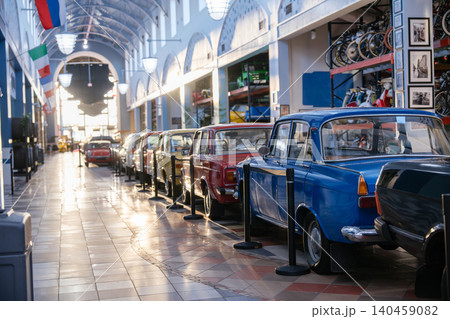 Row of colorful vintage cars displayed inside a bright classic automobile museum with retro architecture and warm sunlight. Historic transportation vehicles and collectible retro automobiles create a 140459082