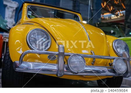 Front view of a yellow vintage Volkswagen Beetle with chrome bumper and classic headlights displayed in a retro car museum. Iconic historic automobile with polished metal details and nostalgic Front view of a yellow vintage Volkswagen Beetle with chrome bumper and classic headlights displayed in a retro car museum. Iconic historic automobile with polished metal details and nostalgic 140459084