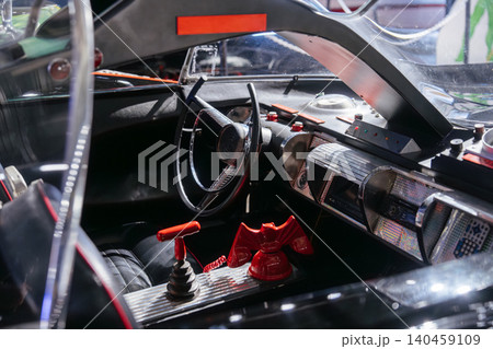Close-up view of vintage car interior featuring a distinctive steering wheel, red gear shift, and unique bat-shaped telephone. Bright lighting highlights chrome accents and retro design elements. Close-up view of vintage car interior featuring a distinctive steering wheel, red gear shift, and unique bat-shaped telephone. Bright lighting highlights chrome accents and retro design elements. 140459109