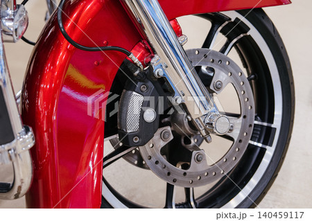Detailed close-up captures front wheel assembly of motorcycle. Vibrant metallic red fender curves over polished chrome front fork, showcasing mechanical components against a blurred background. 140459117