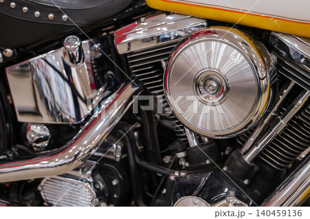 Detailed close-up view showcases motorcycle engine assembly with polished chrome components. Features include ribbed air cleaner, shiny exhaust pipes, and vibrant yellow, white, and orange accents. Detailed close-up view showcases motorcycle engine assembly with polished chrome components. Features include ribbed air cleaner, shiny exhaust pipes, and vibrant yellow, white, and orange accents. 140459136