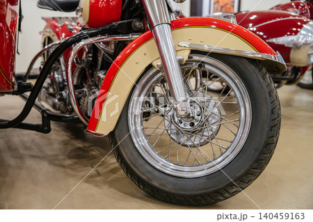 Detailed low-angle view captures front wheel and two-tone cream and red fender of classic motorcycle. Chrome accents and deep-tread tire enhance vintage appeal against polished floor. 140459163