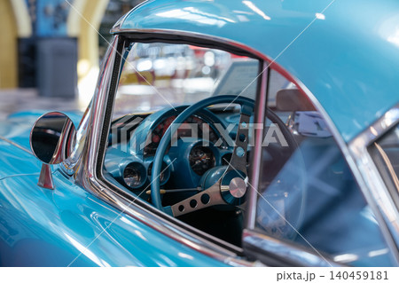 Close-up view of vintage light blue car interior, highlighting vibrant dashboard and steering wheel. Chrome accents and round gauges enhance classic automotive design in softly blurred indoor setting. 140459181