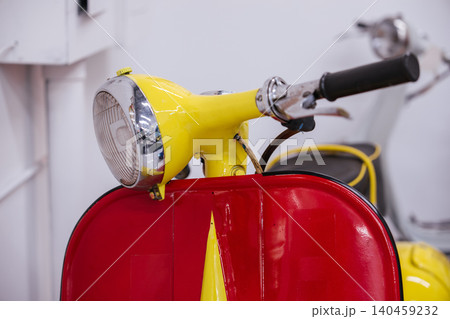 Detailed close-up captures vibrant yellow handlebar and headlight assembly of vintage scooter. Classic design features chrome accents and glossy surfaces, set against a clean white background. Detailed close-up captures vibrant yellow handlebar and headlight assembly of vintage scooter. Classic design features chrome accents and glossy surfaces, set against a clean white background. 140459232