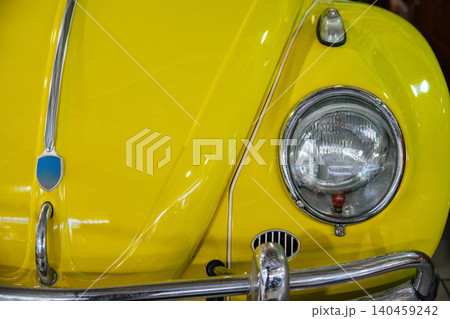 Close-up view captures front detail of vintage yellow car, showcasing glossy paint and chrome accents. Key features include headlight, bumper, and distinctive emblem, highlighting retro design. 140459242