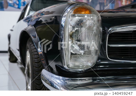 Detailed close-up captures front end of vintage two-tone automobile in black and white. Chrome grille and amber turn signal highlight classic design, reflecting surroundings in bright showroom Detailed close-up captures front end of vintage two-tone automobile in black and white. Chrome grille and amber turn signal highlight classic design, reflecting surroundings in bright showroom 140459247