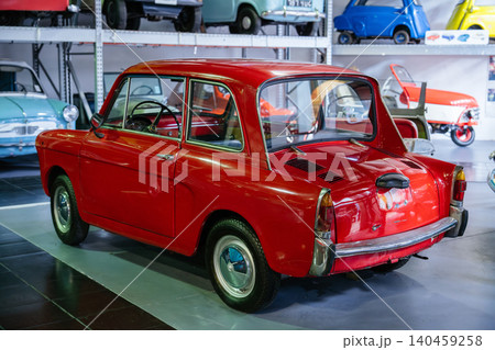 Bright red vintage microcar prominently displayed in a well-organized automotive showroom. Retro design elements and polished interior visible through windows, surrounded by colorful classic cars. Bright red vintage microcar prominently displayed in a well-organized automotive showroom. Retro design elements and polished interior visible through windows, surrounded by colorful classic cars. 140459258