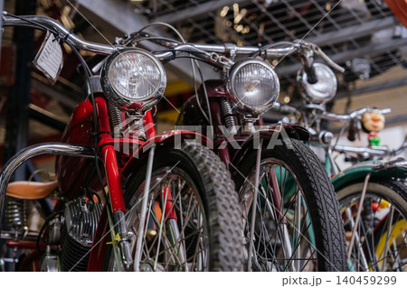 Close-up, low-angle view of vintage motorcycles lined up in workshop. Red motorcycle stands out with chrome handlebars and large headlight, while dark red and green motorcycles are partially visible. 140459299