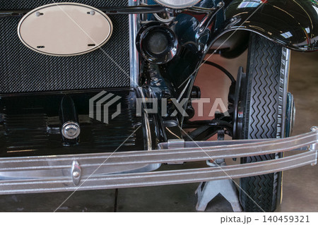 Classic antique car showcases intricate hood ornament and vintage grille in well-lit garage. Nostalgic atmosphere highlights craftsmanship and timeless design. 140459321