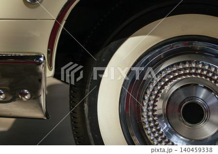 Close-up captures intricate details of vintage car wheel featuring whitewall tire and diamond-patterned chrome hubcap. Chrome bumper showcases visible bolts, evoking a classic and luxurious feel. Close-up captures intricate details of vintage car wheel featuring whitewall tire and diamond-patterned chrome hubcap. Chrome bumper showcases visible bolts, evoking a classic and luxurious feel. 140459338