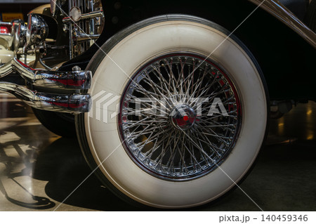 Detailed close-up captures vintage car's whitewall tire and chrome spoked wheel. Polished chrome hub and exhaust pipes reflect surroundings, showcasing classic automotive craftsmanship. Detailed close-up captures vintage car's whitewall tire and chrome spoked wheel. Polished chrome hub and exhaust pipes reflect surroundings, showcasing classic automotive craftsmanship. 140459346