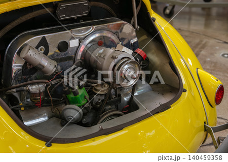 Detailed close-up reveals vintage car engine compartment showcasing intricate mechanical components. Bright yellow exterior frames the exposed engine featuring silver alternator and green distributor Detailed close-up reveals vintage car engine compartment showcasing intricate mechanical components. Bright yellow exterior frames the exposed engine featuring silver alternator and green distributor 140459358