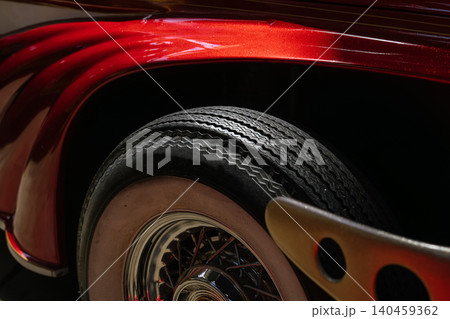 Detailed close-up showcases vintage car's wheel and fender. Vibrant metallic red paint highlights curves, while classic whitewall tire and chrome hub add elegance against a dark background. Detailed close-up showcases vintage car's wheel and fender. Vibrant metallic red paint highlights curves, while classic whitewall tire and chrome hub add elegance against a dark background. 140459362