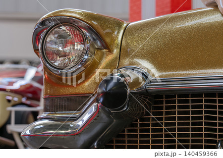 Detailed close-up captures front quarter of vintage automobile featuring shimmering gold glitter paint. Classic round headlight with chrome bezel and polished chrome grille create a striking design. 140459366