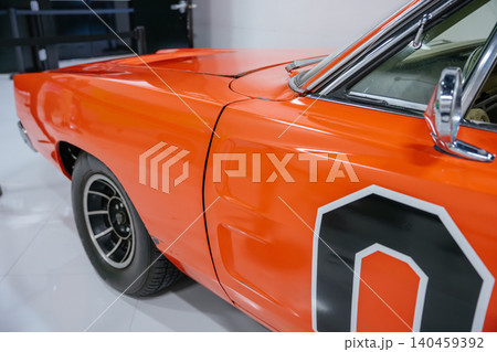 Detailed low-angle view of classic orange car side. Image highlights glossy finish, sharp body lines, and features like fender, door panel, multi-spoke wheel, and chrome side mirror. Detailed low-angle view of classic orange car side. Image highlights glossy finish, sharp body lines, and features like fender, door panel, multi-spoke wheel, and chrome side mirror. 140459392