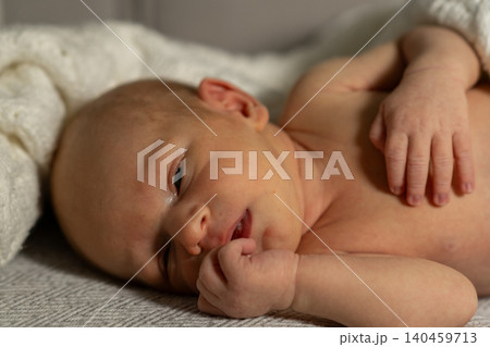 A newborn baby lies on a soft blanket, displaying a serene expression while gently holding a finger in their mouth, radiating innocence and tranquility. A newborn baby lies on a soft blanket, displaying a serene expression while gently holding a finger in their mouth, radiating innocence and tranquility. 140459713