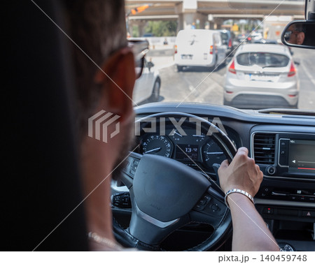 A person is driving a vehicle, navigating through heavy traffic during midday in an urban environment. Other cars are visible on the road. A person is driving a vehicle, navigating through heavy traffic during midday in an urban environment. Other cars are visible on the road. 140459748