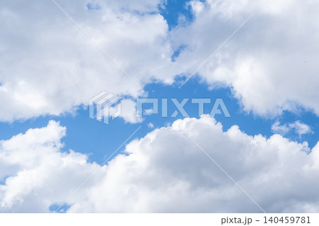 The sky showcases a vibrant blue backdrop filled with soft, fluffy white clouds drifting peacefully above, creating a tranquil atmosphere. 140459781