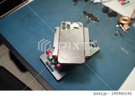 A disassembled smartphone is held in a device on a workbench. Tools and parts are scattered around the setup, showing the repair process in action. 140460148