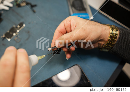 A technician applies adhesive to a smartphone component while working at a repair station in the workshop during daytime. A technician applies adhesive to a smartphone component while working at a repair station in the workshop during daytime. 140460183