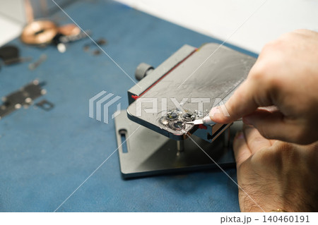 A technician works on a smartphone using tools and components on a workbench in a workshop while applying a repair material. 140460191