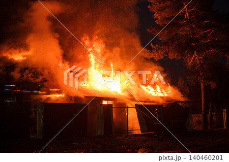 A large fire consumes a structure in a rural setting during nightfall, sending bright flames and thick smoke into the sky. A large fire consumes a structure in a rural setting during nightfall, sending bright flames and thick smoke into the sky. 140460201