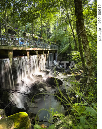 Serene waterfall flows beneath a scenic wooden walkway at Passadicos do Rio Uima in Pigeiros Portugal surrounded by lush tranquil forest greenery Serene waterfall flows beneath a scenic wooden walkway at Passadicos do Rio Uima in Pigeiros Portugal surrounded by lush tranquil forest greenery 140460619