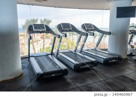 Fitness enthusiasts can enjoy a workout on treadmills while taking in a stunning beach view with palm trees and a serene outdoor space. Fitness enthusiasts can enjoy a workout on treadmills while taking in a stunning beach view with palm trees and a serene outdoor space. 140460967
