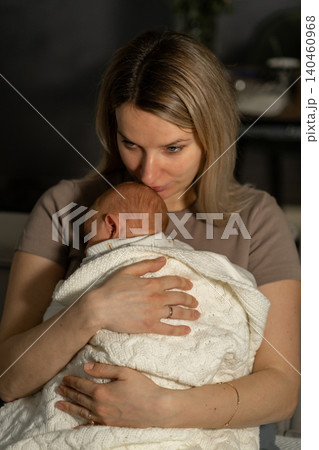 A mother cradles her newborn wrapped in a soft blanket, sharing a tender moment in an intimate home environment as evening light gently illuminates them. A mother cradles her newborn wrapped in a soft blanket, sharing a tender moment in an intimate home environment as evening light gently illuminates them. 140460968