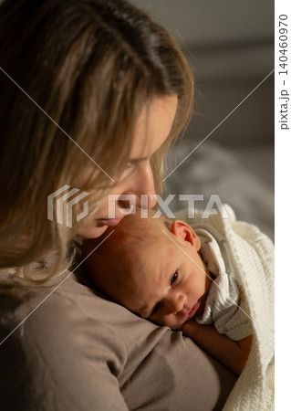 A mother lovingly cradles her newborn baby close while sitting in a cozy setting, sharing a tender moment filled with affection and warmth. 140460970