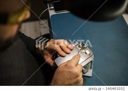 Technician works on a smartphone in a workshop, using tools to fix the device while observing the intricate parts closely. Technician works on a smartphone in a workshop, using tools to fix the device while observing the intricate parts closely. 140461032