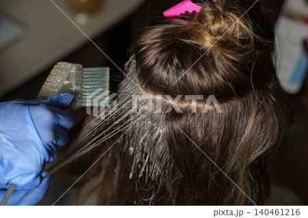 A stylist expertly applies hair dye to long, dark hair in a salon, showcasing a focus on the coloring process with tools in hand and casual surroundings. A stylist expertly applies hair dye to long, dark hair in a salon, showcasing a focus on the coloring process with tools in hand and casual surroundings. 140461216