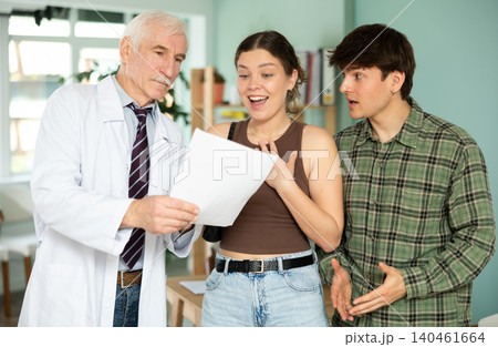 Happy young couple listening elderly doctor's explanations about test results Happy young couple listening elderly doctor's explanations about test results 140461664