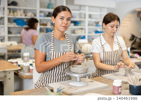 Two young women pottery workshop workers sculpt from raw clay Two young women pottery workshop workers sculpt from raw clay 140461986