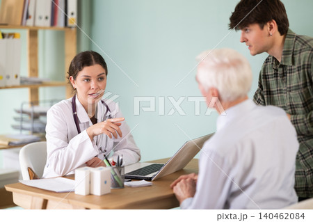 Senior man next to his adult son sits in the doctors office 140462084
