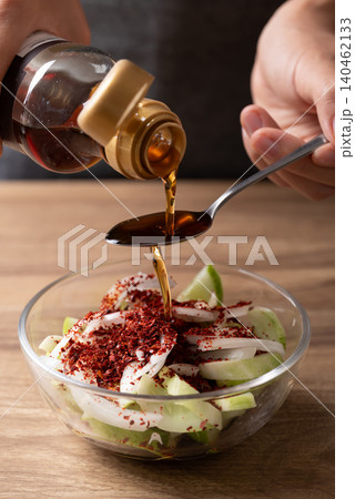 Woman hand pouring sesame oil into a bowl with cucumber to making cucumber salad Woman hand pouring sesame oil into a bowl with cucumber to making cucumber salad 140462133