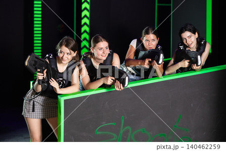 Four positive girlfriends playing enthusiastically laser tag in dark room Four positive girlfriends playing enthusiastically laser tag in dark room 140462259