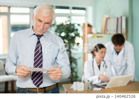 Elderly man holds prescriptions in his hands in the doctors office. 140462526