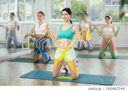 Young girls doing arm workout with resistance band standing on knees 140462544
