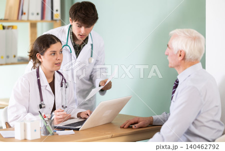 Elderly man is sitting in a medical office, he consults with two young doctors Elderly man is sitting in a medical office, he consults with two young doctors 140462792